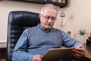 älterer Mann, der Nachrichten auf digitalem Tablett liest foto