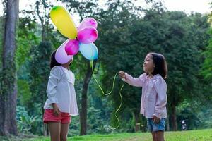 zwei Kind Mädchen halten bunt Spielzeug Luftballons im das Park draußen. foto