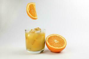 frisch Gelb Orange Saft im Glas mit ganze schwebend geschnitten Orange Obst und Eis Würfel auf Weiß Hintergrund foto