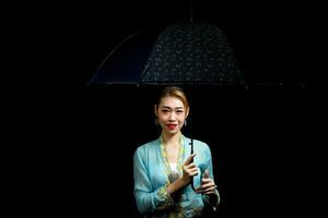 asiatisch Frau im Zugkraft Kebaya Tragen Regenschirm auf schwarz Hintergrund foto