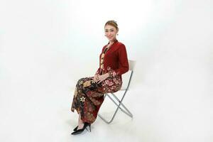 asiatisch Frau traditionell rot kastanienbraun Kebaya Sharong auf Weiß Hintergrund Sitzung Pose Stuhl sitzen foto