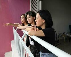 jung Süd-Ost asiatisch Frau Gruppe auf Balkon Veranda Stehen Seite durch Seite genießen Aussicht reden glücklich suchen foto