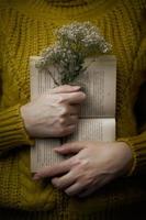 Frau im Pullover hält Buch und Blumenstrauß foto