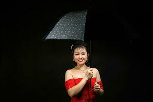 asiatisch Frau im modern rot Kleid unter Regenschirm auf schwarz Hintergrund foto