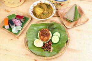 nasi Lemak duftend Reis Kokosnuss Milch mit Sambal Freund Erdnuss Anschovis Ei verpackt Banane Blatt runden Bambus Teller bunt Nyonya kuih Süss Wüste Palme Blatt Teller auf hölzern Hintergrund foto