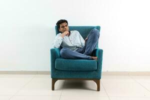 ein jung Süd Osten asiatisch sitzen Pose aussehen denken Arbeit Studie Emotion Gefühle auf ein Blau Single Sofa. er ist adhd und autistisch foto