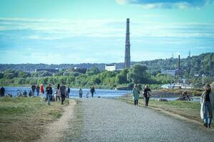 Kaunas, Litauen 20 10 2022 Menschen Gehen auf ein Beton Pfad in der Nähe von Fluss Blau Wasser auf hell sonnig Tag mit Blau Himmel und szenisch Aussicht foto