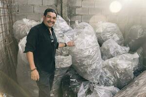 Mann lächelnd und suchen beim Kamera zeigen seine Recycling arbeiten, Taschen voll von Plastik Flaschen. foto