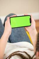 jung Mädchen Sitzung auf ein Sofa und mit ein Smartphone mit Grün Bildschirm foto