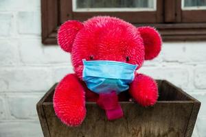 einsamer roter Teddybär in einer medizinischen Schutzmaske foto