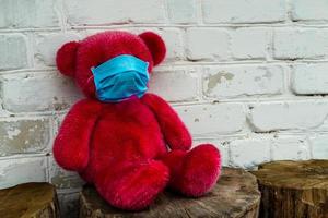 einsamer roter Teddybär in einer medizinischen Schutzmaske foto