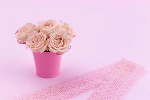 Ein Strauß schöner Rosen steht in einem kleinen Eimer an einem Spitzenband foto