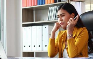 Porträt der asiatischen Frau im gelben Anzug, der im Büro sitzt und über Marketing nachdenkt foto