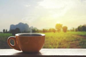 heißer schwarzer heißer Kaffee mit Rauch auf einem Holztisch mit einer Naturlandschaft mit Berg foto