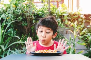 Das süße asiatische Kind zeigte einen guten Ausdruck, als es eine Pizza auf einem Teller sah foto