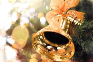 goldene Glocken mit einer roten Schleife auf einem Weihnachtsbaum, verwischen hellen Bokehhintergrund