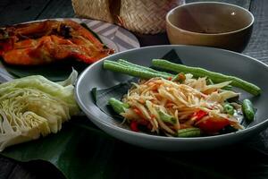 thailändisch Essen Gericht beide im Thailand und Asien, Papaya Salat oder wie wir Anruf es somtum ist ergänzt mit gegrillt Hähnchen und klebrig Reis mit frisch Pfannengerichte. serviert auf das schwarz hölzern Tisch. foto