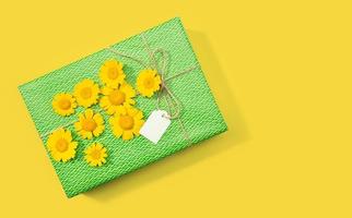Geschenk- oder Geschenkbox mit leerem Etikett und Gänseblümchenblumen auf gelbem Hintergrund kopieren Raumoberansichtmodell foto