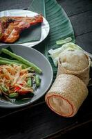 thailändisch Essen Gericht beide im Thailand und Asien, Papaya Salat oder wie wir Anruf es somtum ist ergänzt mit gegrillt Hähnchen und klebrig Reis mit frisch Pfannengerichte. serviert auf das schwarz hölzern Tisch. foto