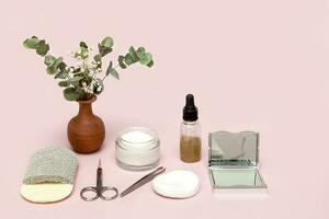 Schönheit Zubehör zum Selbstpflege Schere, Pinzette, Gesichts- Schwamm, Serum, Spiegel, Creme, Baumwolle Pads, Vase mit Blumen auf ein Rosa Hintergrund foto