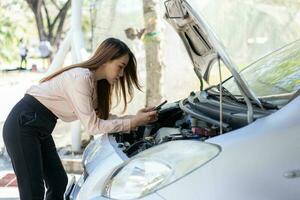 wütend asiatisch Frau mit ein Smartphone Video Konferenz zum Hilfe nach ein Auto Nervenzusammenbruch auf Straße. Konzept von ein Fahrzeug Motor Problem oder Unfall und Notfall Hilfe von ein Fachmann Mechaniker foto