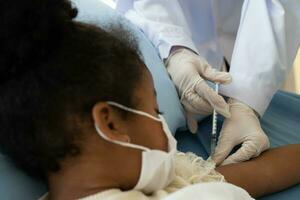 asiatisch Arzt Benutzer Spritze Nadel zum Injektion impfen, afrikanisch amerikanisch Kinder sind Sein covid geimpft zum Verhütung Coronavirus und Grippe. Konzept von Immunisierung von Impfung foto