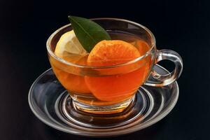 Flüssigkeit Tee Zitrone Orange Scheibe Grün Blatt Zimt Stock im transparent Glas Teetasse Untertasse auf schwarz Hintergrund foto