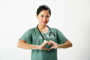 jung asiatisch weiblich Arzt tragen Schürze Uniform Tunika Stethoskop aussehen beim Kamera Hart Hand singen foto