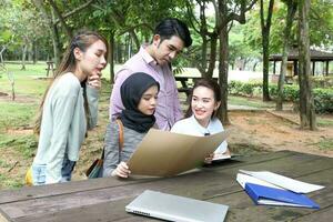 jung asiatisch malaiisch Chinesisch Mann Frau draussen Park Buch Datei Mappe Laptop Computer Telefon sitzen Stand Studie mischen foto