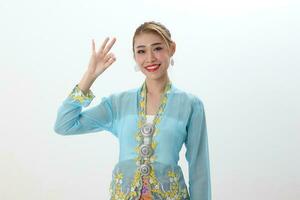 asiatisch Frau traditionell Blau Orange Kebaya Sharong auf Weiß Hintergrund Finger in Ordnung singen foto