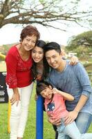 Süd-Ost asiatisch Mehrgenerationen Familie Eltern Tochter Oma Vater Mutter Kind Pose glücklich sitzen Stand draussen Park foto
