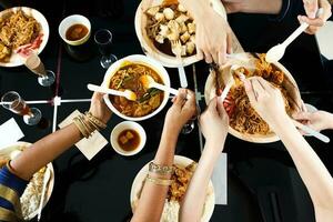 jung Süd-Ost asiatisch Frau Gruppe sich unterhalten feiern Essen genießen Essen Reis Curry Nudel Hähnchen trinken Prost auf Essen Tabelle oben Aussicht foto