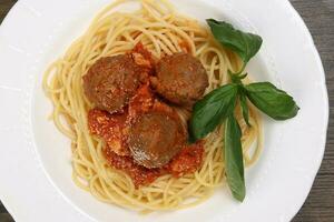 gekocht Spaghetti Tomate Frikadelle Soße Käse Pulver Basilikum auf Weiß Teller hölzern Tabelle foto