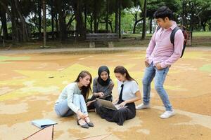 jung asiatisch malaiisch Chinesisch Mann Frau draussen Park sitzen auf Boden Studie sich unterhalten diskutieren Punkt Laptop Datei Buch Rucksack mischen Spaß Treffen foto