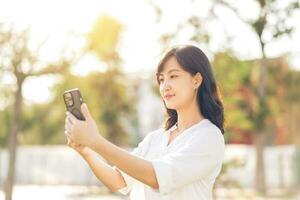 Porträt schön jung asiatisch Frau mit Clever Handy, Mobiltelefon Telefon um draussen Natur Aussicht im ein sonnig Sommer- Tag foto