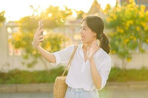 Porträt jung schön asiatisch Frau mit Smartphone zu Video Anruf mit Freund und erkunden Straße auf Sommer- Ferien im Bangkok, Thailand foto