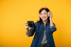 Porträt jung asiatisch Frau mit glücklich Erfolg Lächeln tragen Denim Kleider halten Joystick Regler und spielen Video Spiel. Spaß und entspannen Hobby Unterhaltung Lebensstil Konzept. foto