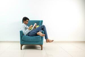 ein jung Süd Osten asiatisch sitzen Pose aussehen denken Arbeit Studie Emotion Gefühle auf ein Blau Single Sofa. er ist adhd und autistisch foto