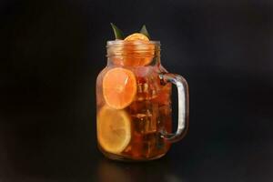 Flüssigkeit Eis Zitrone Orange Tee mit Scheibe Grün Blatt Zimt Stock im transparent Glas Krug Becher auf schwarz Hintergrund foto