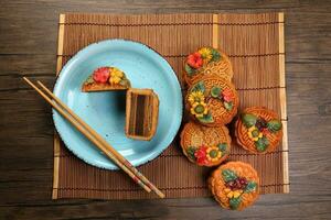 bunt Blume dekoriert Mondkuchen Chinesisch Mitte Herbst Festival Schnitt Scheibe auf Blau Keramik Teller Hintergrund auf Bambus Essen Matte foto