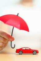 Geschäftsfrau hält roten Regenschirm und deckt rotes Autospielzeug auf dem Tisch ab. autoversicherung, garantie, reparatur, finanz-, bank- und geldkonzept foto