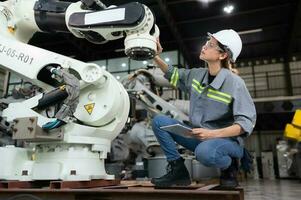 ein weiblich Ingenieur installiert ein Programm auf ein Robotik Arm im ein Roboter Lagerhaus. und Prüfung das Betrieb Vor Senden das Maschine zu das Kunde. foto