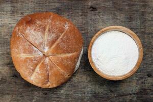 frisch gebacken Brot Laib runden mit Mehl im hölzern Schüssel auf rustikal Holz Hintergrund foto