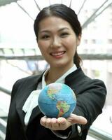 Süd-Ost asiatisch jung Büro Geschäft Frau tragen passen halten Globus Welt Karte auf Palme von ihr Hand beim draussen Lokal foto