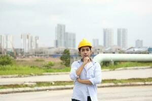 asiatisch Mann malaiisch Arbeiter Ingenieur Verwaltung schwer Hut Sicherheit Helm beim Konstruktion Seite? ˅ Stand Denken Hand auf Kinn foto