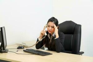 jung asiatisch weiblich tragen passen Sitzung beim Büro Schreibtisch auf Telefon Denken Hand im Stirn foto