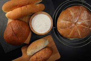 frisch gebacken Brot Laib Brötchen rollen runden lange mischen Wahrheit Mehl im hölzern Schüssel auf hölzern Tafel Metall Grill Über schwarz Hintergrund foto