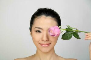 jung schön Süd-Ost asiatisch Frau Schönheit Mode bilden Licht grau Weiß Hintergrund halten Rosa Rose Über Auge Gesicht foto