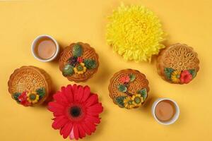 bunt Blume dekoriert Mond Kuchen Chinesisch Mitte Herbst Tee im klein Teetasse Festival Gänseblümchen Chrysantheme Mama Blume rot Gelb Rosa lila violett auf Gelb Hintergrund foto