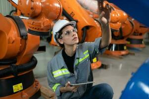 ein weiblich Ingenieur installiert ein Programm auf ein Robotik Arm im ein Roboter Lagerhaus. und Prüfung das Betrieb Vor Senden das Maschine zu das Kunde. foto